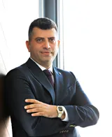 Op. Dr. Cenk Teker, ear, nose and throat surgeon, standing by a window in a navy suit